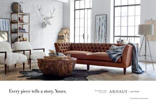 Living room interior showcasing a tufted brown leather sofa, a unique wooden coffee table, and two white fluffy chairs against a white brick wall.
