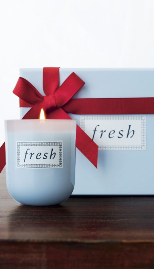 Fresh-branded light blue candle next to a matching gift box tied with a red ribbon, set on a dark wood surface against a white background.