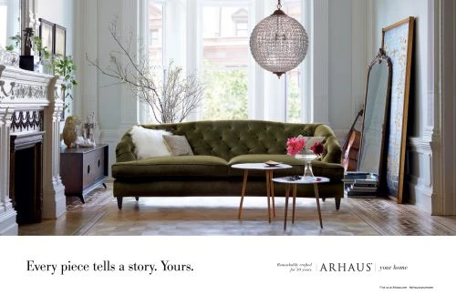 Tufted green velvet sofa in a bright living room with large windows, a crystal globe chandelier, and a decorative fireplace.
