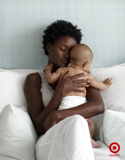 A tender portrait of an African-American woman cradling a baby in a bed, showcasing intimate mother-child bonding with soft lighting.