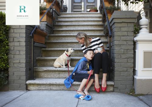 Woman, boy, and dog sitting on front steps of house. Woman is holding a white mug, boy is wearing a cape and holding a leash.