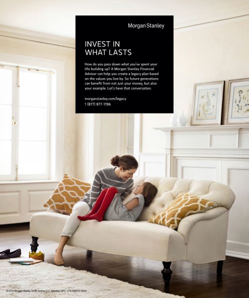 A mother and daughter are relaxing together on a white chaise lounge indoors near a window in a lifestyle financial service advertisement.