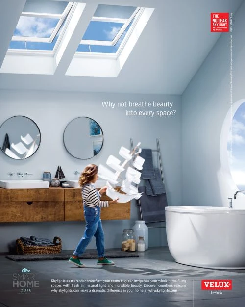 A child in a bright, modern bathroom is holding a construction of white paper; skylights provide natural light. Velux ad.