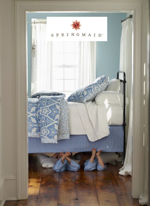 Whimsical scene of children's feet under a blue-and-white bed in a sunlit room. Brand logo 'Springmaid' is centered at the top.