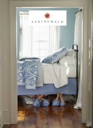 Whimsical scene of children's feet under a blue-and-white bed in a sunlit room. Brand logo 'Springmaid' is centered at the top.