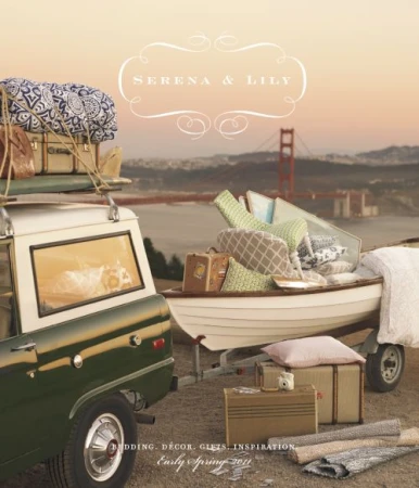 Vintage green and white car towing a boat trailer full of bedding, pillows and luggage near the Golden Gate Bridge at sunset.