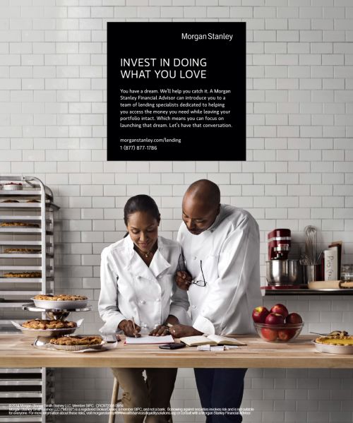 Two chefs, an African-American woman and man, review recipe in a commercial kitchen with pies, bowls of apples, and kitchen equipment.