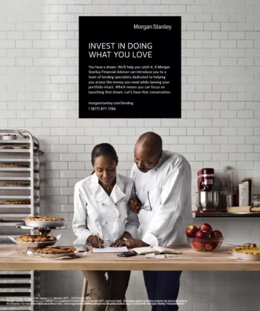 Two chefs, an African-American woman and man, review recipe in a commercial kitchen with pies, bowls of apples, and kitchen equipment.