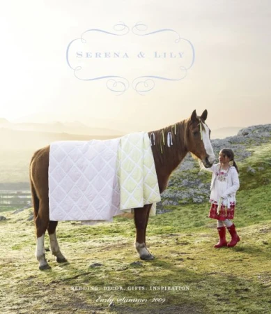 A young girl in red boots stands beside a brown horse draped in quilted pastel blankets in a grassy rural landscape at sunset.