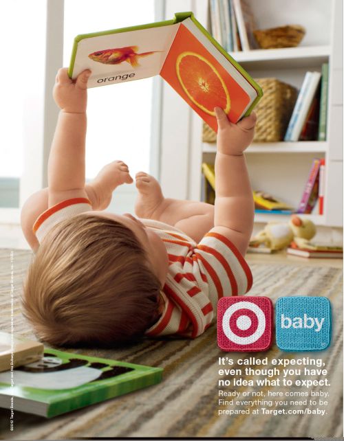 Infant lies on striped rug holding a baby book open to an orange fruit illustration. Other baby books are on the carpet.