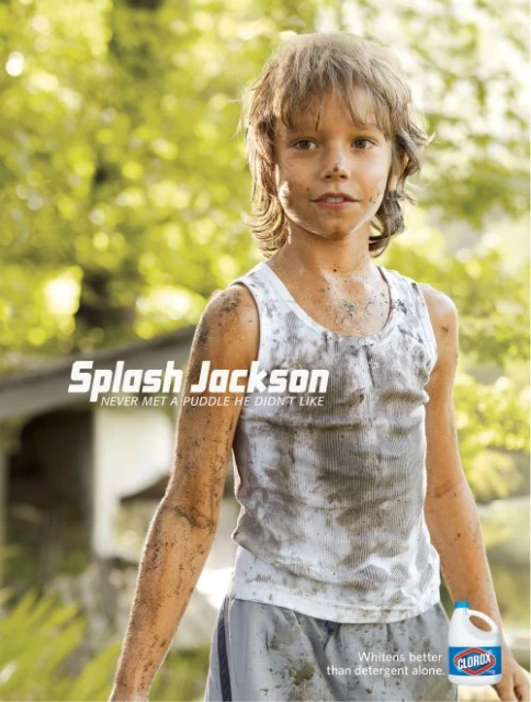 Young boy covered in dirt wearing a white tank top and light-colored shorts stands outdoors in an advertisement for Clorox.