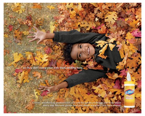 Child lies smiling amid colorful fall leaves with a bottle of Clorox wipes. Bright and cheerful scene.