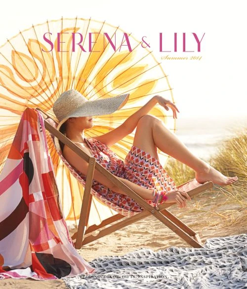 Woman in floral dress and sunhat lounges in a wooden deck chair on the beach under a large parasol, promoting summer apparel.