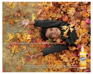 Smiling child lying in a large pile of golden autumn leaves with arms outstretched, photographed by Laurie Frankel.