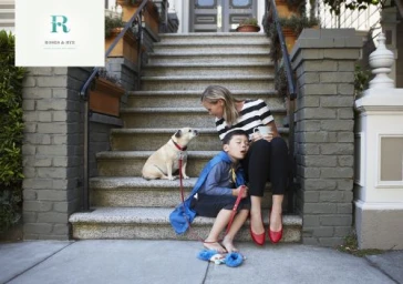 A woman and a young boy in a blue cape seated on stone front steps next to a pug dog, photographed by Laurie Frankel.