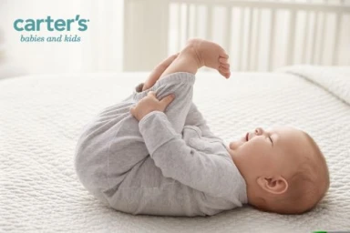 Baby lying on back on a quilted white bed holding feet up in the air