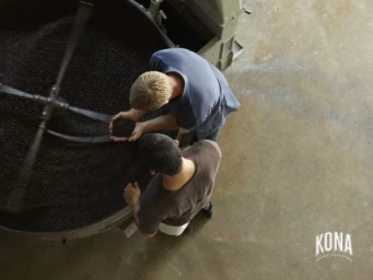 High angle shot of two men examining roasted coffee beans in a large industrial roaster by Laurie Frankel