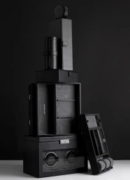 A tower of stacked black leather watch boxes and cases against a dark background, photographed by Laurie Frankel.