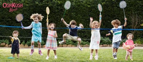 Group of children jumping and holding badminton rackets in a grassy park setting by photographer Laurie Frankel