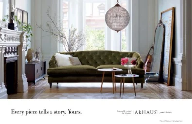 Tufted green velvet sofa in a bright living room with large windows, a crystal globe chandelier, and a decorative fireplace.