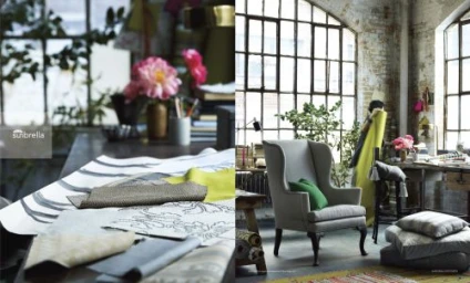 Interior shot featuring a light grey wingback armchair with green pillows in a sunlit loft workspace by Laurie Frankel