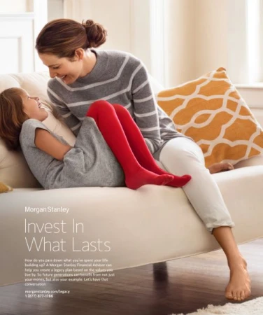 Woman in grey striped sweater and young girl in red tights laughing together on a white sofa, photographed by Laurie Frankel