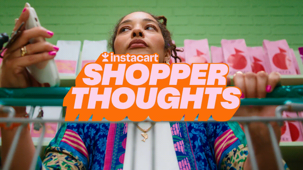 An adult female in a patterned jacket stands in a grocery store aisle with pink packaged goods visible on the shelves in the background.