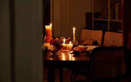 Warmly lit dinner table with burning candles, dishes of food, and woven chairs creates a cozy indoor atmosphere.