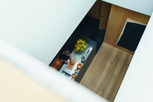 Overhead view of a woman in a modern kitchen preparing food at the counter with flowers, wooden bowls, and kitchenware.