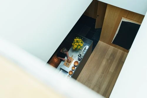 Overhead view of a woman in a modern kitchen preparing food at the counter with flowers, wooden bowls, and kitchenware.