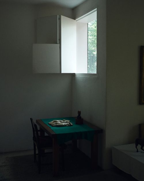 Interior room featuring a wooden table under a window with white shutters, with sculpture and items laid on green cloth.