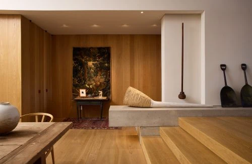 Interior view of living space with blonde wood walls and floors, a concrete block, and decorative elements in soft, diffused light.