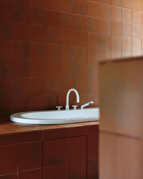 White oval ceramic sink with silver faucet set against a warm brown tiled wall and countertop in a modern bathroom.