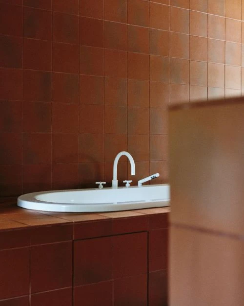 White oval ceramic sink with silver faucet set against a warm brown tiled wall and countertop in a modern bathroom.