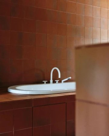 White oval ceramic sink with silver faucet set against a warm brown tiled wall and countertop in a modern bathroom.