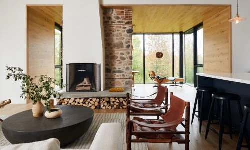 Living room interior featuring a stone fireplace, firewood, leather sling chairs, oval coffee table with plant decor, and modern furniture.
