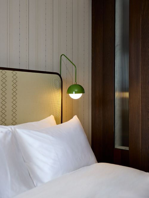 Interior view of a bedroom featuring a bed with white linens and a green dome-shaped lamp mounted on the wall, creating a cozy atmosphere.