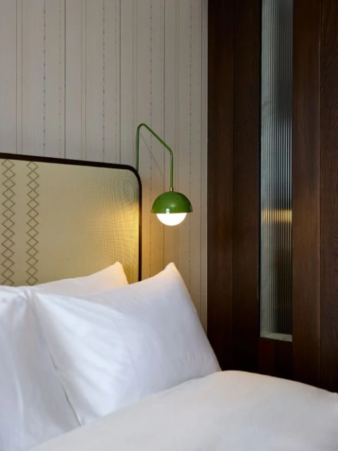 Interior view of a bedroom featuring a bed with white linens and a green dome-shaped lamp mounted on the wall, creating a cozy atmosphere.