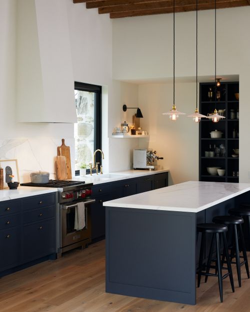 Modern kitchen interior with blue cabinetry, white countertops, wooden floors, pendant lighting, stainless steel appliances, and minimal decor.