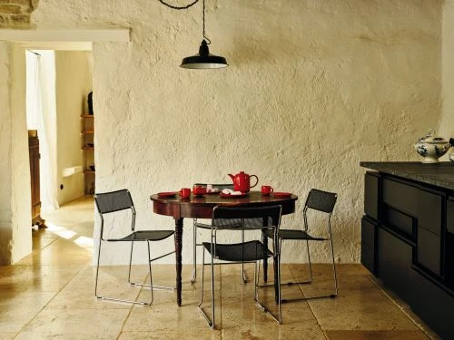 Indoor shot of a kitchen with a round dining table set for tea, featuring four metal chairs, granite countertops, and natural light.