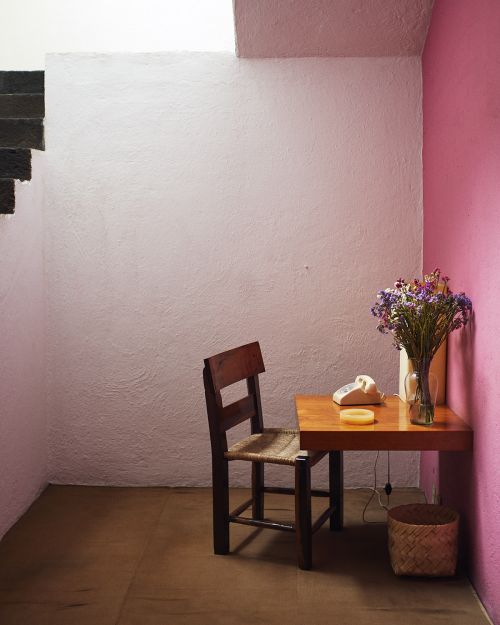 Interior scene with a wooden chair and table in a corner, topped with dried flowers, telephone, plus a woven basket on a wood floor.