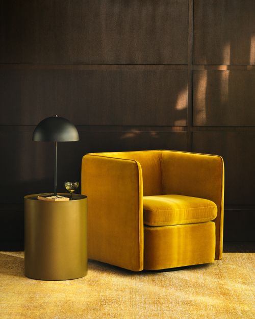 Interior design featuring a mustard yellow velvet armchair on a matching carpet, accented by a round side table and modern lamp.
