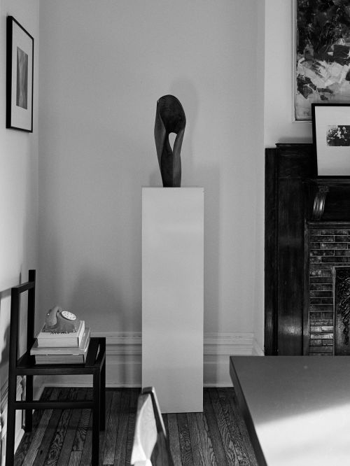 Interior view of a modern sculpture on a white pedestal, vintage telephone on a chair, and artwork hanging on the walls.