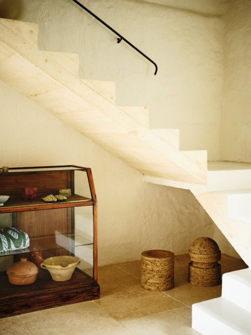 Indoor shot of a staircase with a dark railing, a display cabinet with dishware, and decorative stools, creating a warm and inviting ambiance.