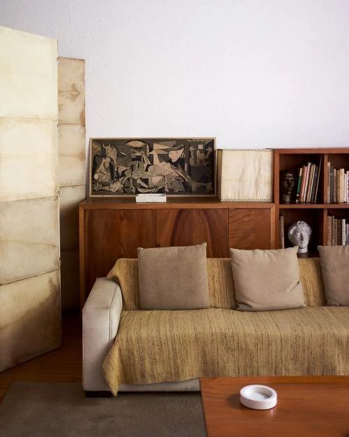 Interior shot of a living room featuring a couch with pillows, a wooden cabinet, artwork, and books creating a cozy, inviting atmosphere.
