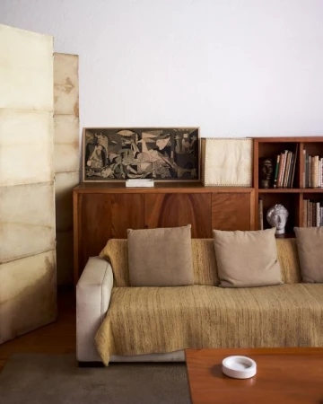 Interior shot of a living room featuring a couch with pillows, a wooden cabinet, artwork, and books creating a cozy, inviting atmosphere.