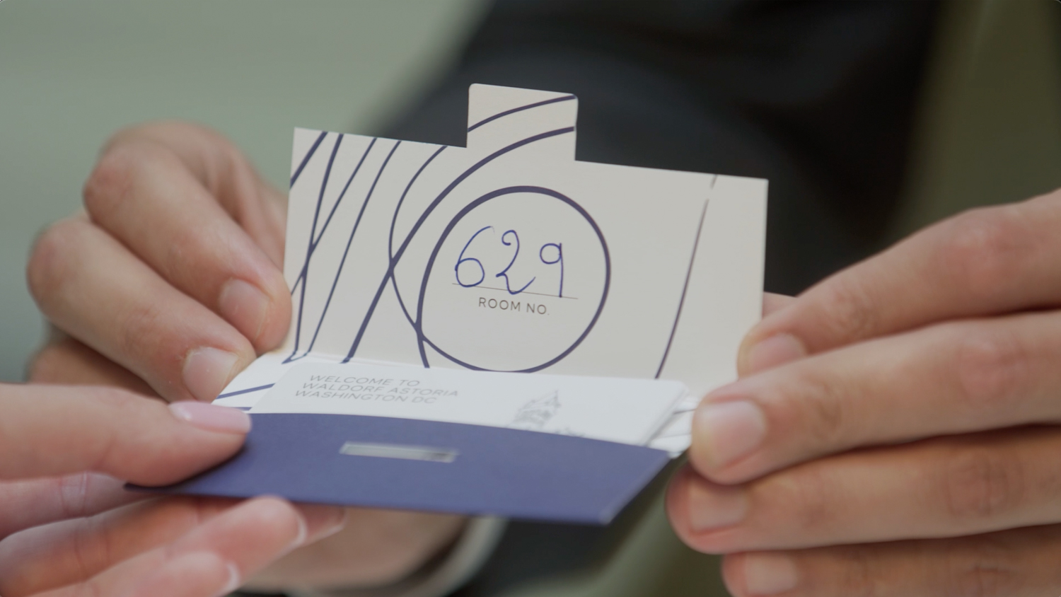 Close-up of hands presenting a hotel room key card for room 629 at Waldorf Astoria Washington DC, emphasizing hospitality and travel.