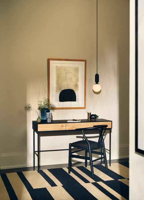 Interior design shot of a minimal desk setup with a black desk chair, abstract wall art, and a pendant light in a neutral room.