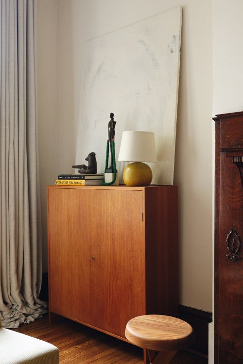 Interior shot of mid-century modern cabinet with art, lamp, and decor in a warmly lit home setting, next to a wooden side table.