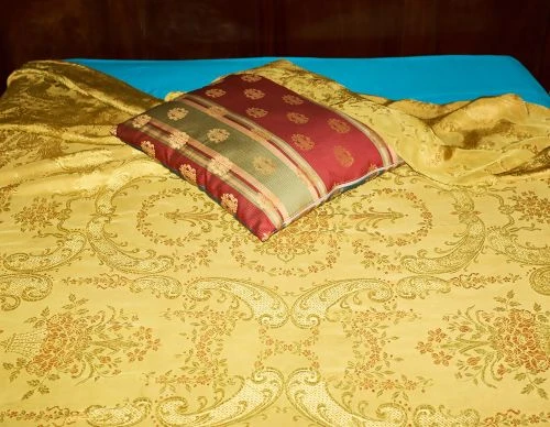 Bedroom interior features a gold floral-patterned bedspread, a red decorative pillow, and a turquoise sheet against a dark wooden headboard.